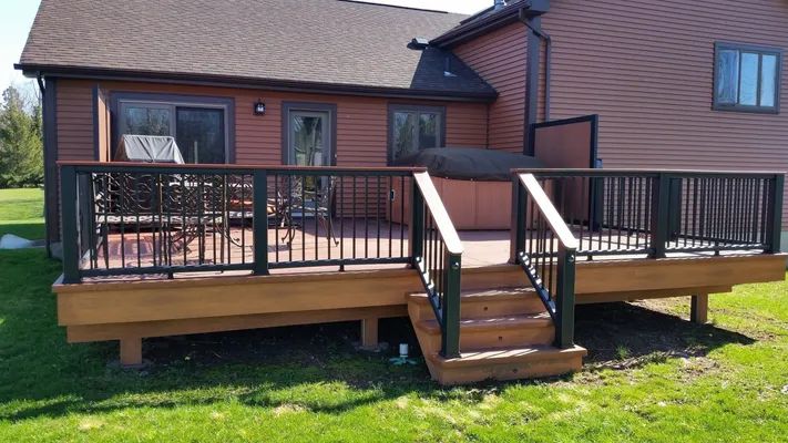 Wooden deck with black railings and steps leading down to a grassy yard.