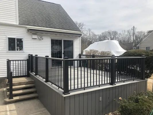 Composite deck with black railing and steps leading to a house with sliding glass doors and white siding.