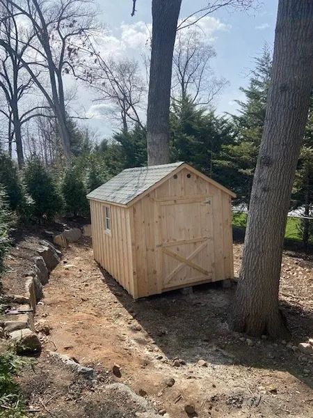 Wooden shed with a gable roof, built in a yard with trees.
