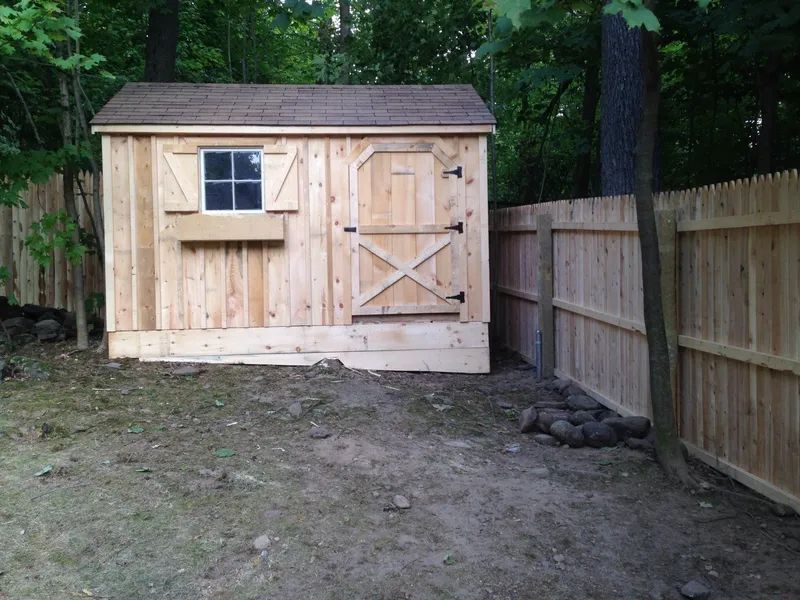 Wooden shed with window, door, and flower box; set in a backyard, beside a fence.