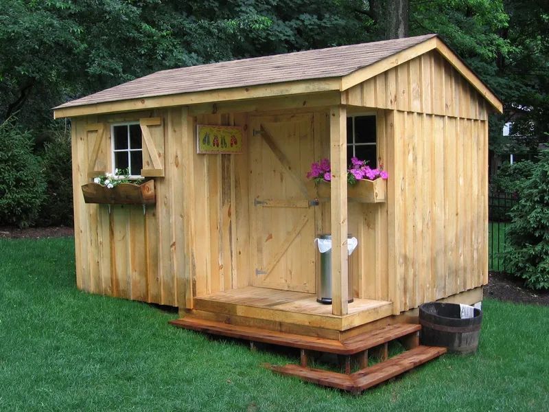 Wooden shed with a small porch, windows with flower boxes, and a barrel on the lawn.