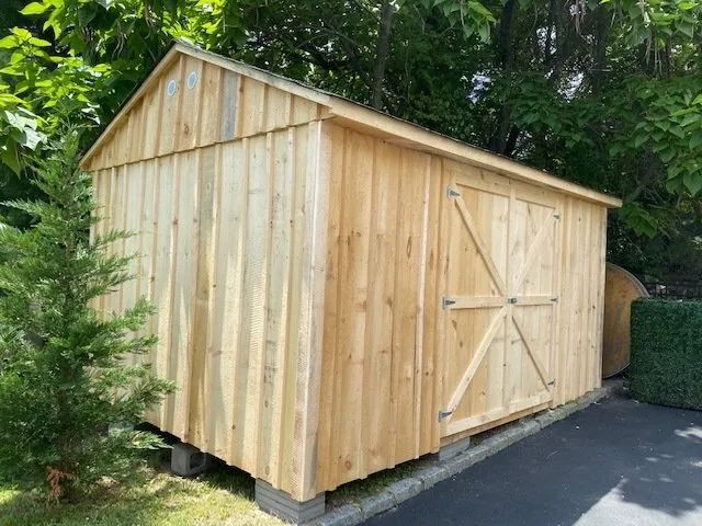 Wooden storage shed with a gabled roof and a door, set in a yard.
