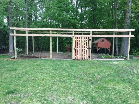 A wooden chicken coop with a fenced enclosure in a grassy backyard.