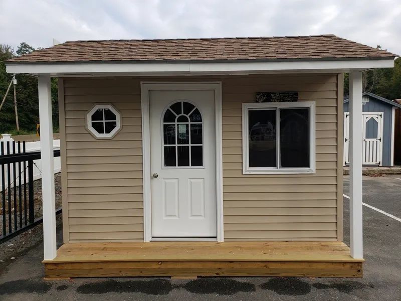 Tan shed with brown roof, white door, windows, and porch.