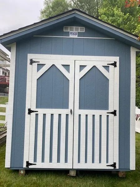 Blue shed with white trim and doors on a grassy lawn.