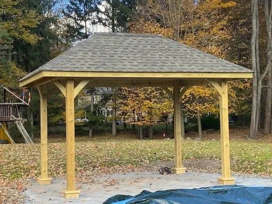 Wooden gazebo with shingled roof in a yard.