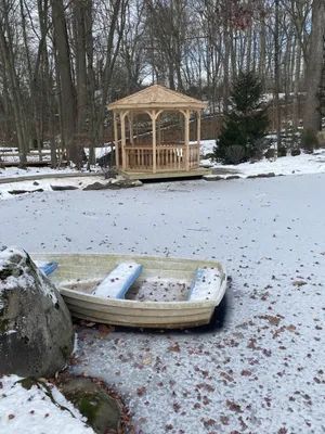 A wooden gazebo and boat on a frozen pond in a snowy outdoor setting.