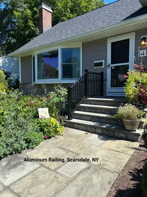 Exterior view of a house with stone steps, a black aluminum railing, and a garden.