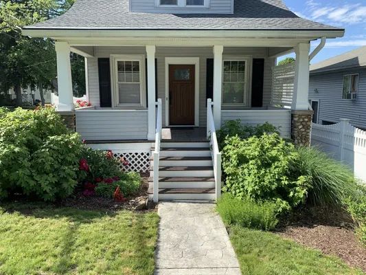 Gray house with porch, steps, and landscaping. A walkway leads to the front door.