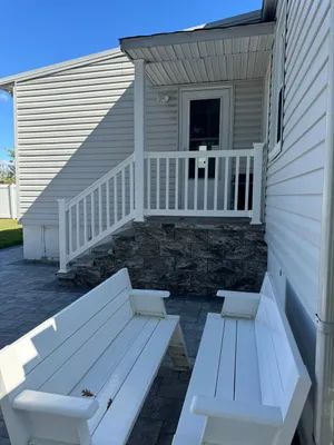 White benches on a patio face a raised porch with white railings, steps, and a back door.