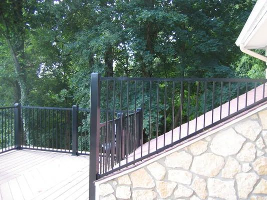 Black metal railing on a deck with stone wall, overlooking green trees.