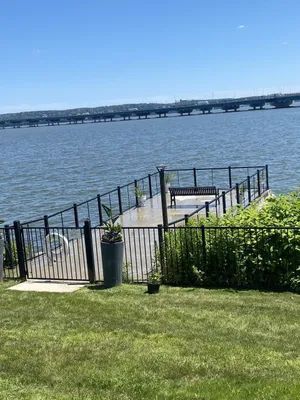 Wooden dock with black railing on a body of water. A bridge is in the distance.