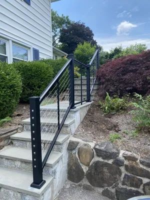 Black metal handrails with cable infill on stone steps leading up to a house.