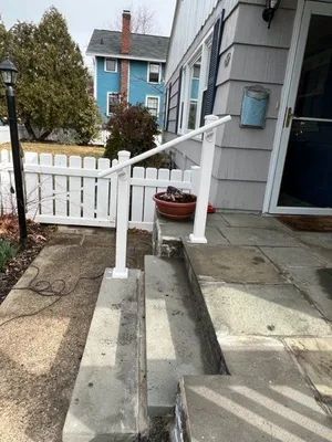 Concrete steps with white railing leading to a house entrance. White picket fence in front.