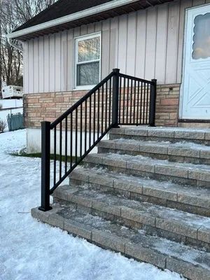 Black railing on stone steps leading to a house entrance; snow on the ground.