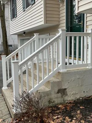 White railing and steps leading up to the front door of a house with light tan siding.
