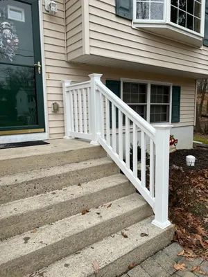 White railing alongside concrete steps leading up to a house with beige siding and green shutters.