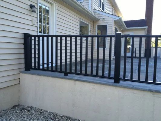 Black railing atop a concrete wall in front of a light-colored house.