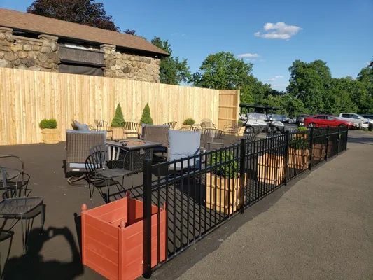 Outdoor dining area with tables, chairs, and planter boxes. A wooden fence surrounds the area.