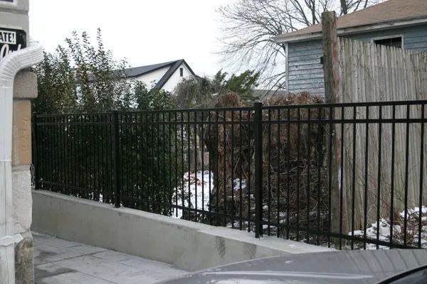 Black metal fence along a cement wall in a residential setting.