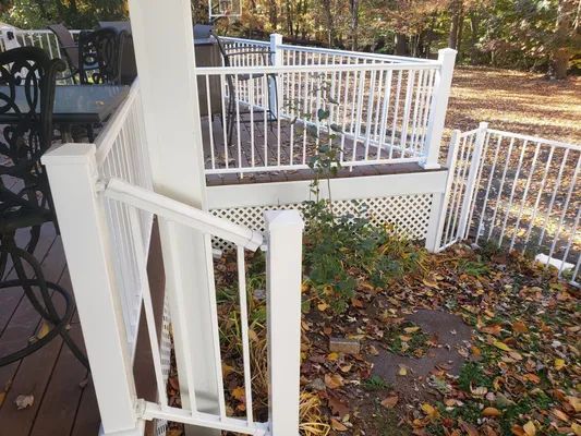 White deck railing with a gate, on a wooden deck with lattice skirting, surrounded by leaves.