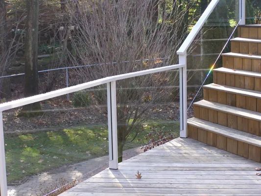 Glass and white metal railing on wooden deck with stairs in a wooded area.