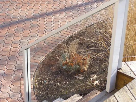 Glass railing on a deck and stairs overlooking a brick patio and garden.