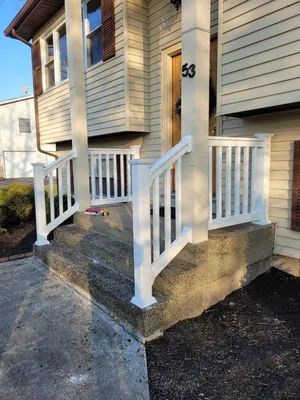 White railing and columns on a house porch with concrete steps.