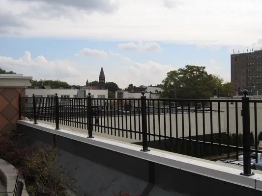 Black railing on a rooftop overlooking rooftops and a distant church steeple under a cloudy sky.