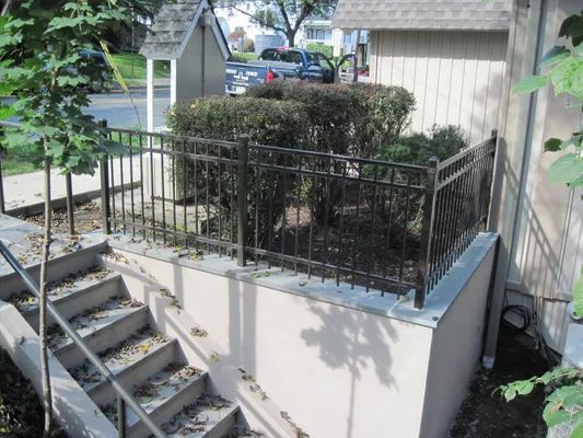 Exterior view of stairs leading down, metal railing, bushes behind a metal fence.