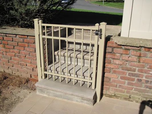 Gate over stairs, beige metal frame, brick wall backdrop.