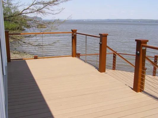 Wooden deck with brown railing, stainless steel cables, overlooking water.