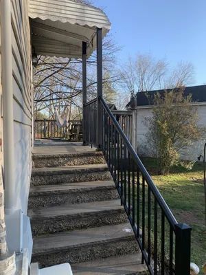 Concrete steps leading up to a porch with black railing and canopy. Wooden siding house in background.