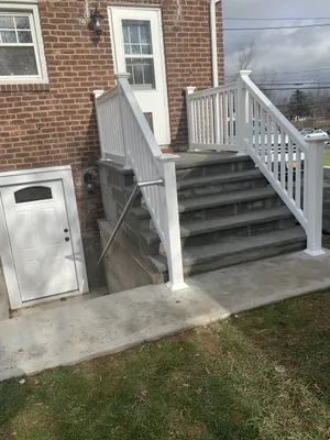Exterior view of brick house with concrete stairs and white railing leading to a door. A white door is on the left side.