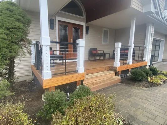 Wooden porch with white columns, black railings, and double doors.
