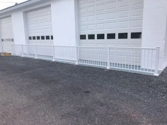 White fence in front of a white building with garage doors. Black gravel ground.