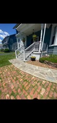 Blue house with white trim and a stone walkway. Brick path leads to the house.