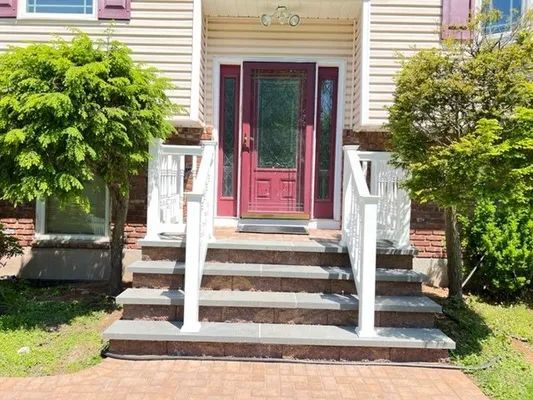A house entrance with three steps, red door, white railings, and flanking green bushes.