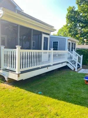 White deck with railing, stairs, and screened porch attached to a house with a blue exterior and green lawn.