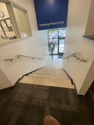 Staircase leading down from an office entrance. White walls, metal handrails, and a carpeted landing.