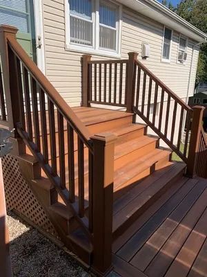 Wooden deck with brown steps and railing leading to a house with beige siding.