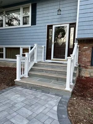 Blue house with white railing and steps leading to the front door, with a stone walkway.