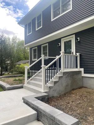 Exterior of a two-story house with dark siding. Steps lead to a white door. Concrete and black railing.