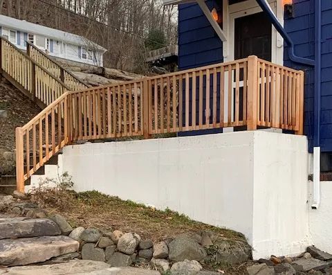 Wooden railing and steps leading up to a blue house with a white base.