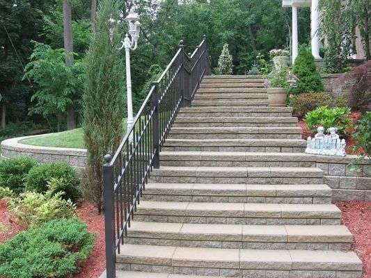 Stone steps with black railing leading up to a house surrounded by landscaping and trees.