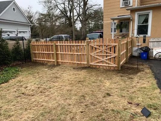 A wooden fence with a gate encloses a backyard; brown grass and a house are visible.