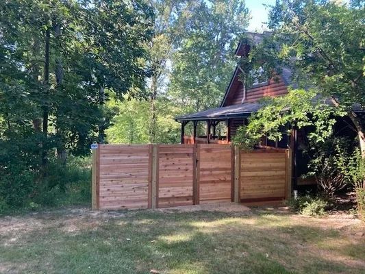 Wooden fence with a gate in front of a cabin, set in a wooded area.