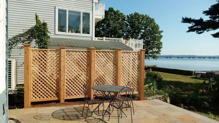 Patio with lattice fence, table, chairs, and view of water.