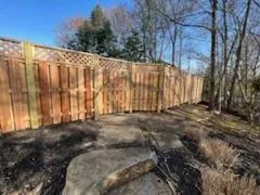 Wooden fence with lattice top in a natural setting. Brown wood, blue sky, and rocks in foreground.