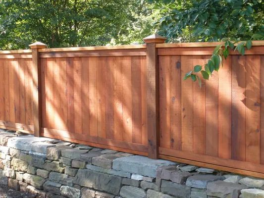 Wood fence with decorative posts atop a stone wall, surrounded by foliage.